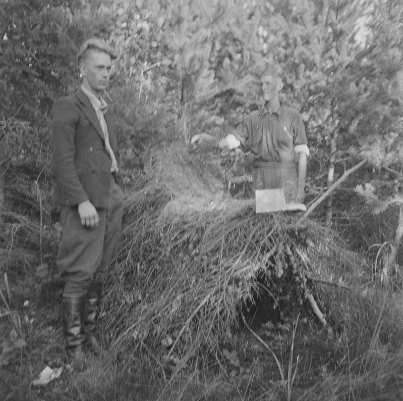 Must-valge pilt kahest mehest metsas, kus nad seisavad künka juures, mille all on metsavendade punker.
